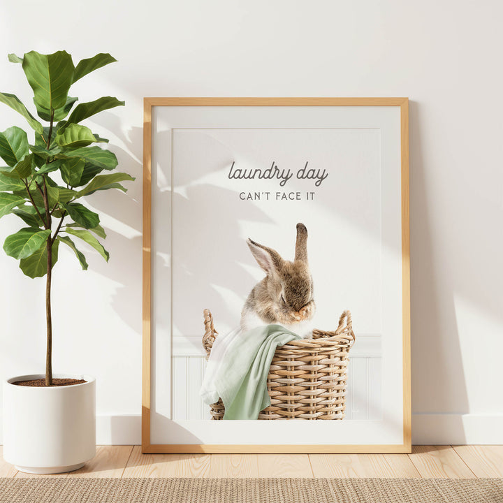 A framed image of a rabbit sitting in a wicker basket, with the text "laundry day can't face it" written above the rabbit.