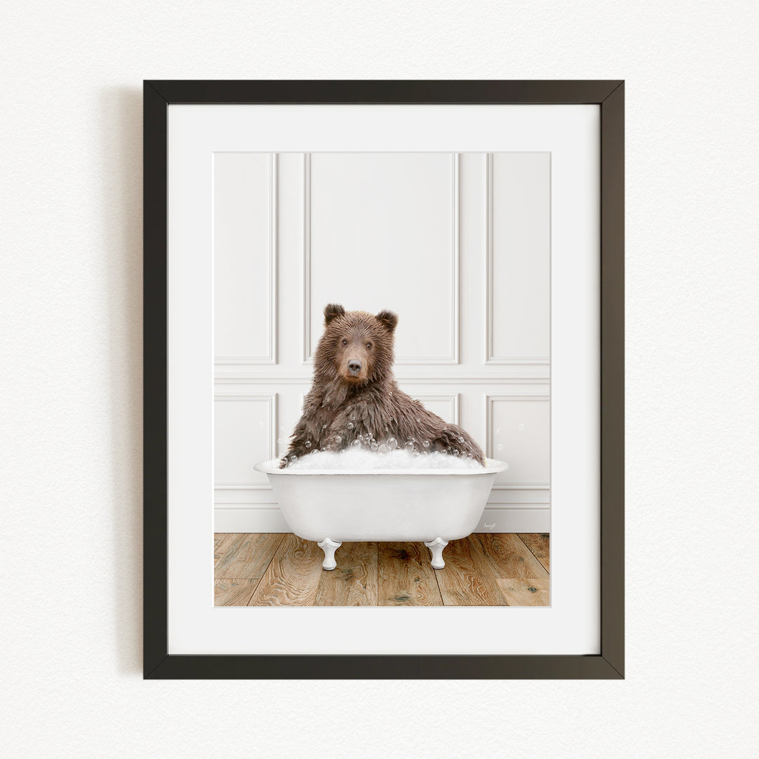 A brown bear sitting in a white bathtub filled with water, with a wooden floor in the background.