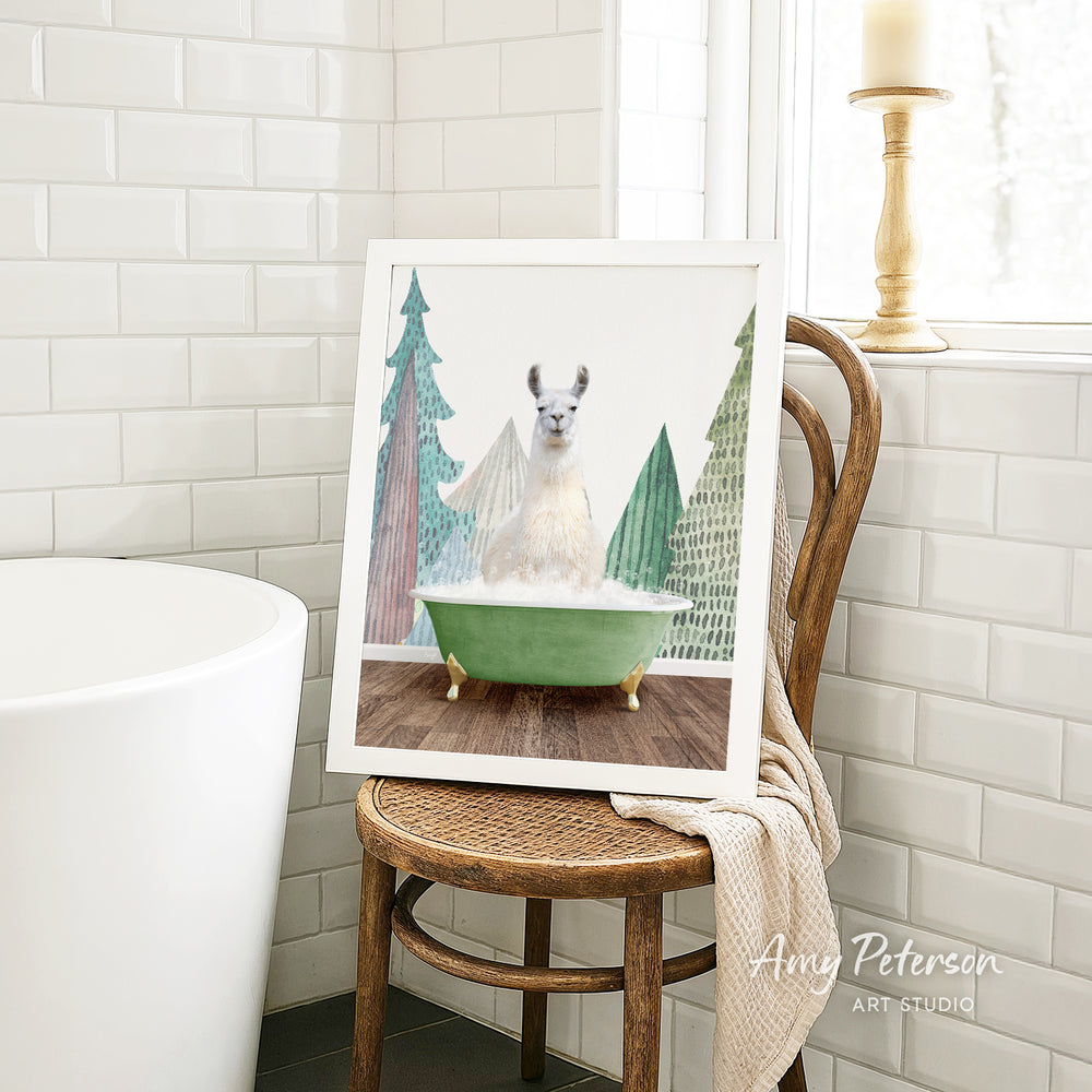 A framed image of a white llama sitting in a green bathtub, surrounded by Christmas trees, is displayed on a wooden chair in a bathroom setting.