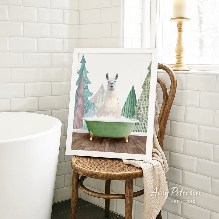 A framed image of a white llama sitting in a green bathtub, surrounded by Christmas trees, is displayed on a wooden chair in a bathroom setting.
