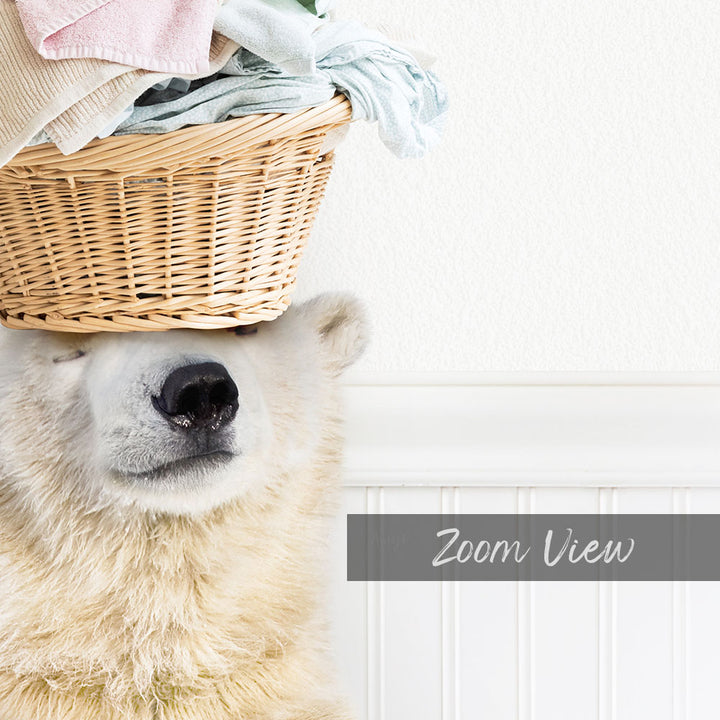 A polar bear is sitting on a wicker basket filled with laundry, with the bear's eyes closed and appearing to be in a relaxed state.