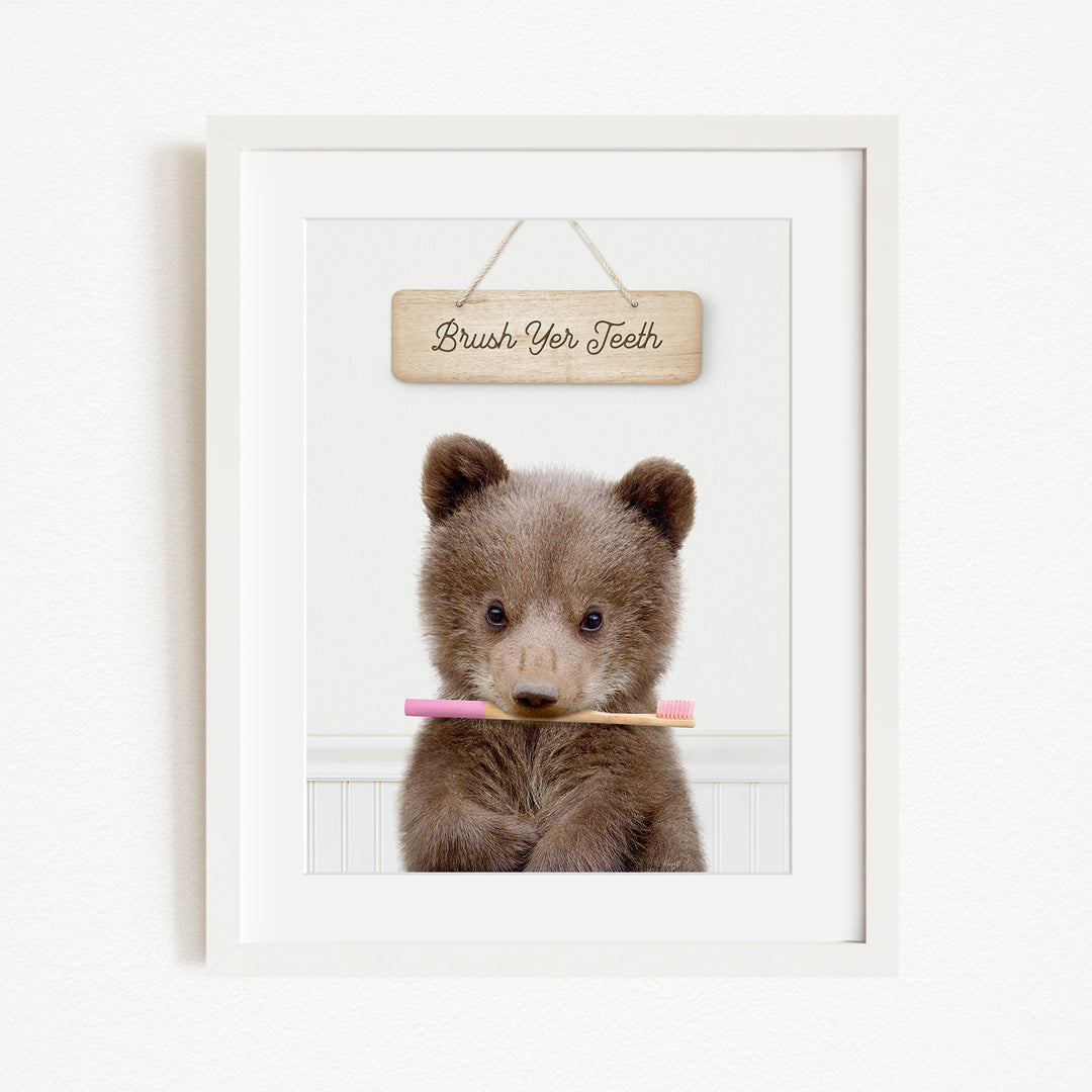 A cute brown bear holding a pink toothbrush in front of a wooden sign that says "Brush Your Teeth".