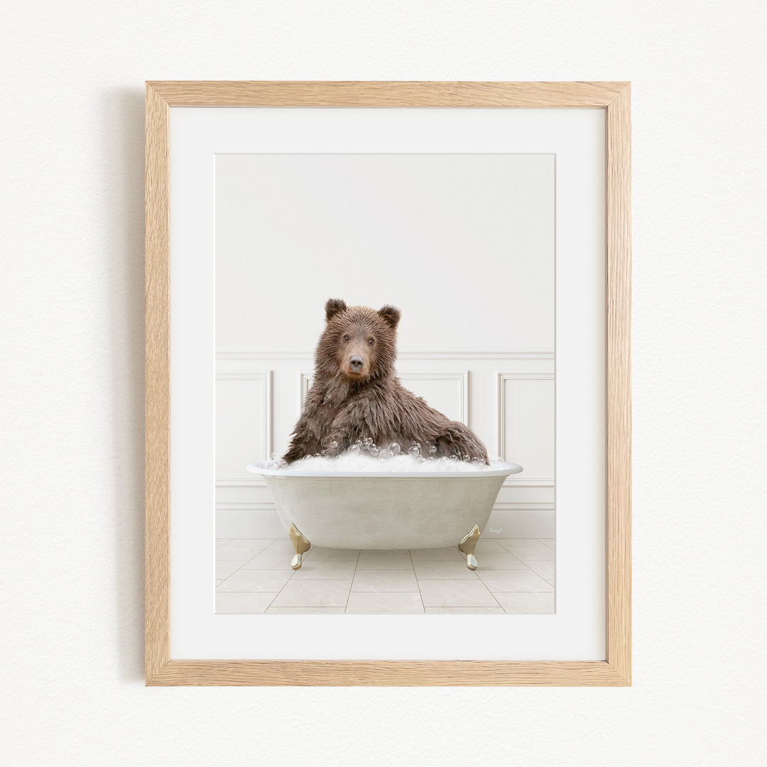 A brown bear sitting in a white bathtub filled with bubbles, looking directly at the camera.