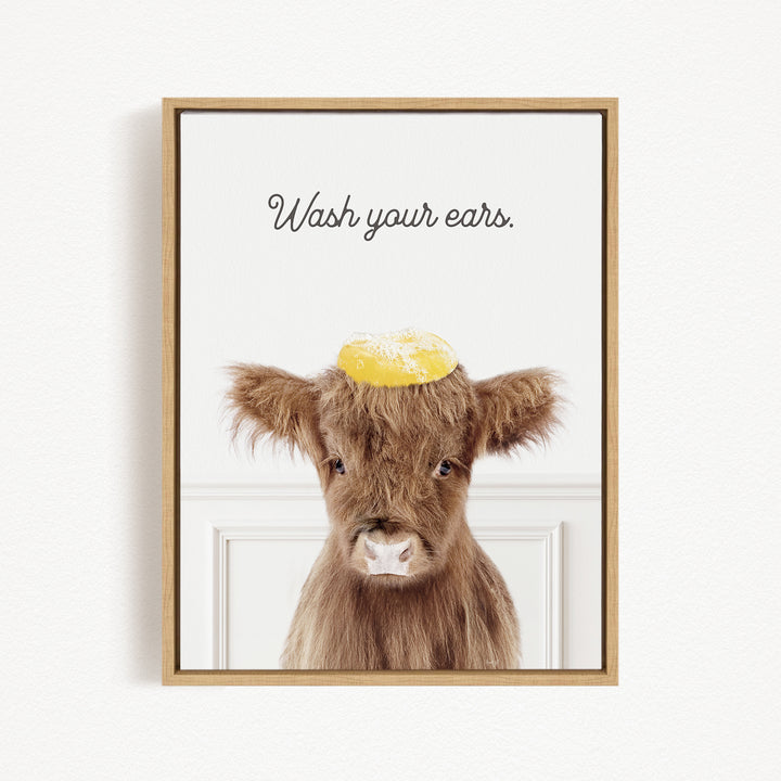 A framed image of a brown cow with a yellow object on its head, accompanied by the text "Wash your ears."