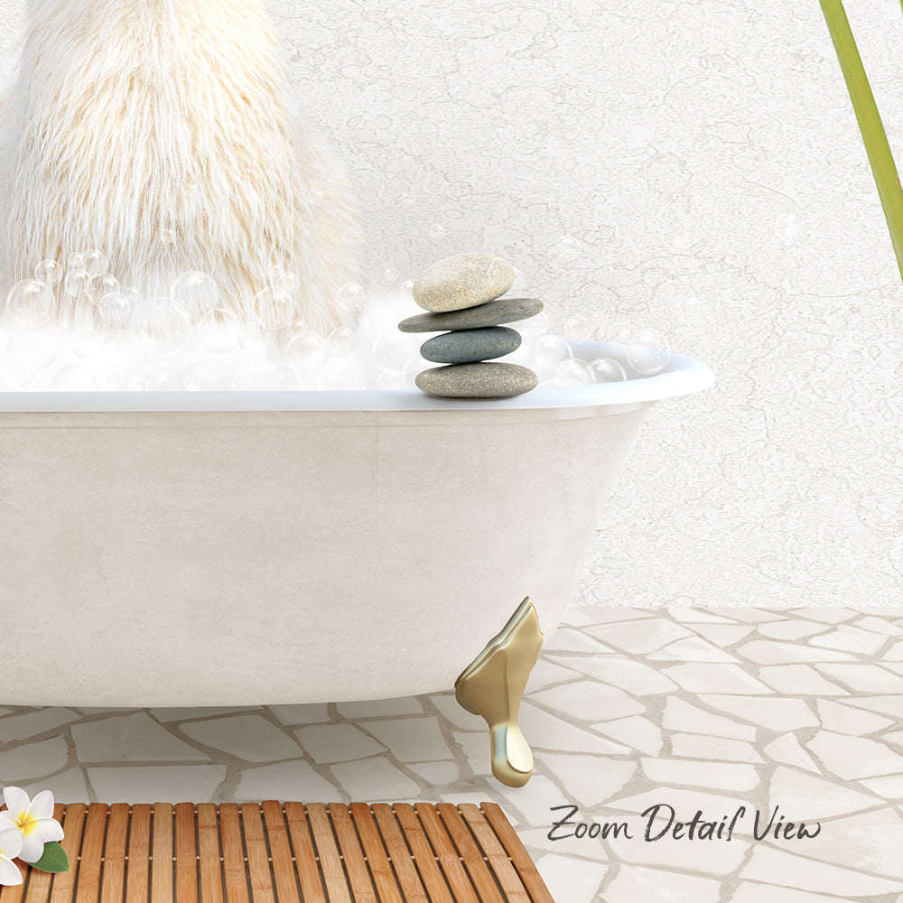 A white bathtub filled with bubbles, with a stack of rocks on the edge and a wooden mat on the floor.