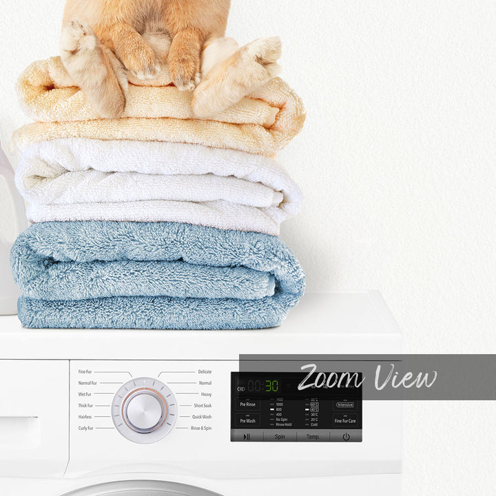 A stack of folded towels on top of a white washing machine, with a digital display and control panel visible.