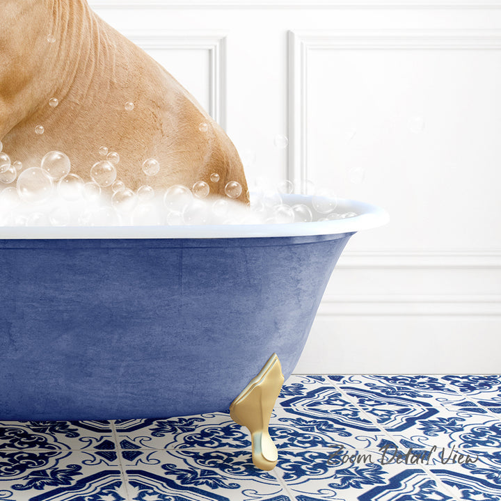 A dog is sitting in a blue bathtub filled with bubbles, with a gold claw-like object on the floor next to the tub.