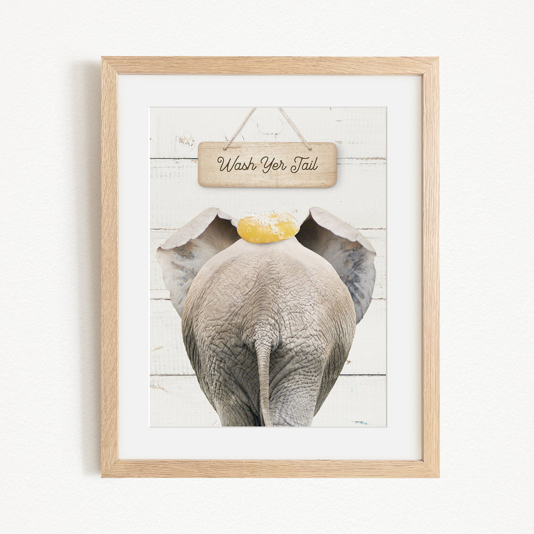 A framed image of an elephant with a sign that says "Wash Your Tail" hanging above it.