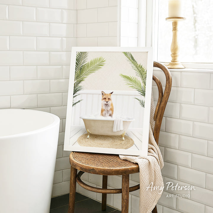 A framed image of a fox sitting in a bathtub, surrounded by palm leaves, is displayed on a wooden chair in a bathroom setting.