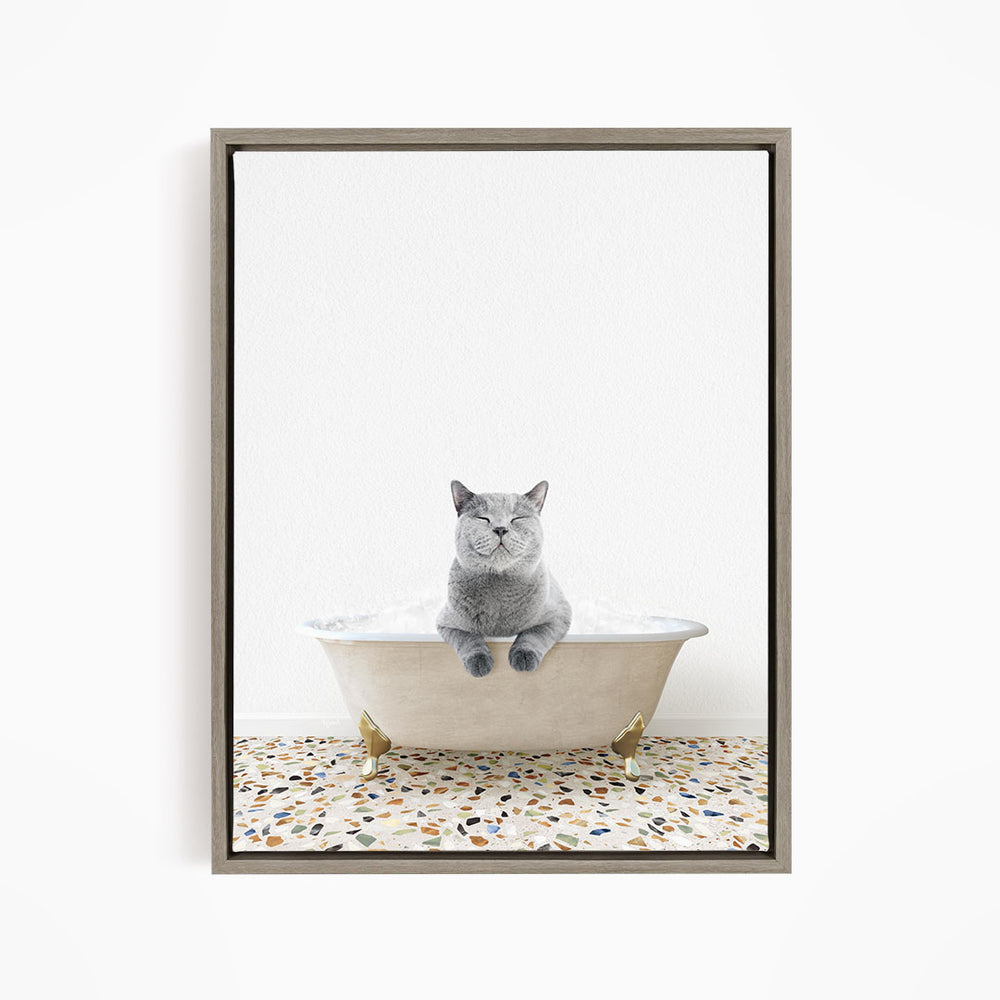 A gray cat sitting in a white bathtub filled with bubbles, with a speckled floor in the background.