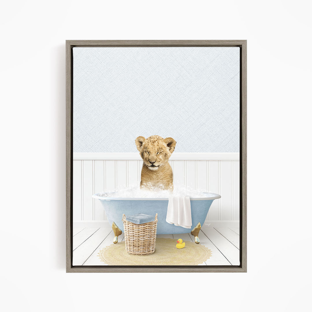 A young lion cub sitting in a blue bathtub filled with water, surrounded by a basket of toys and a yellow rubber duck.