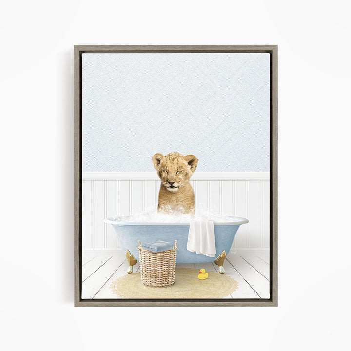 A young lion cub sitting in a blue bathtub filled with water, surrounded by a basket of toys and a yellow rubber duck.