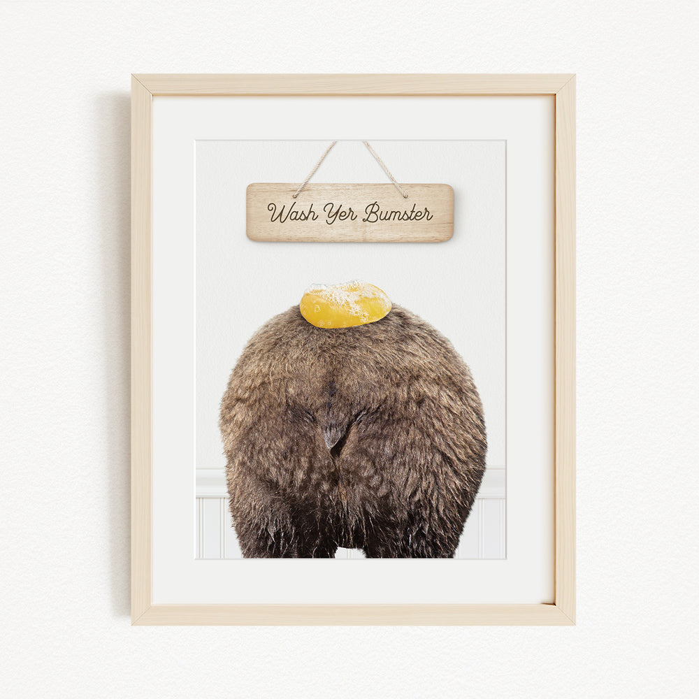 A framed image of a bear with a yellow object on its head, accompanied by a wooden sign that says "Wash Your Bummer".
