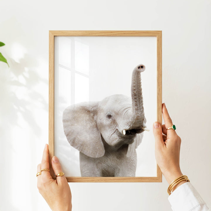 A person's hands are holding a wooden frame with a picture of a gray elephant inside it.