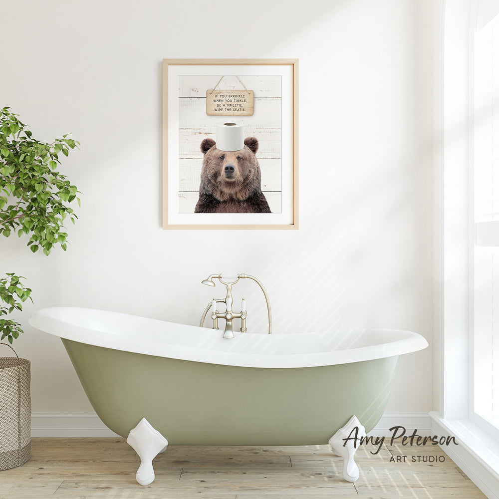 a framed picture of a brown bear with a humorous caption above it, hanging on a white wall above a green clawfoot bathtub.