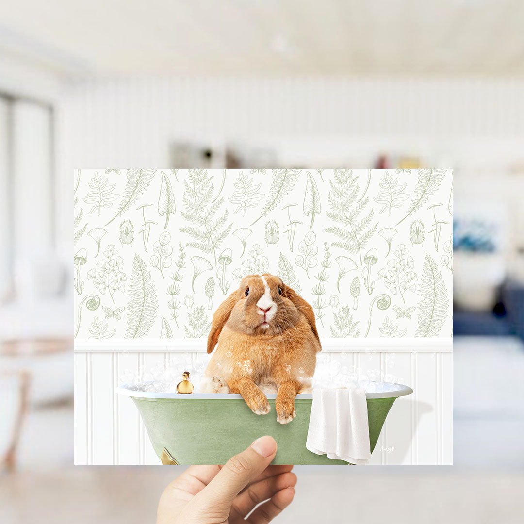 A hand holding a framed image of a rabbit sitting in a bathtub filled with bubbles, surrounded by a green and white floral pattern.