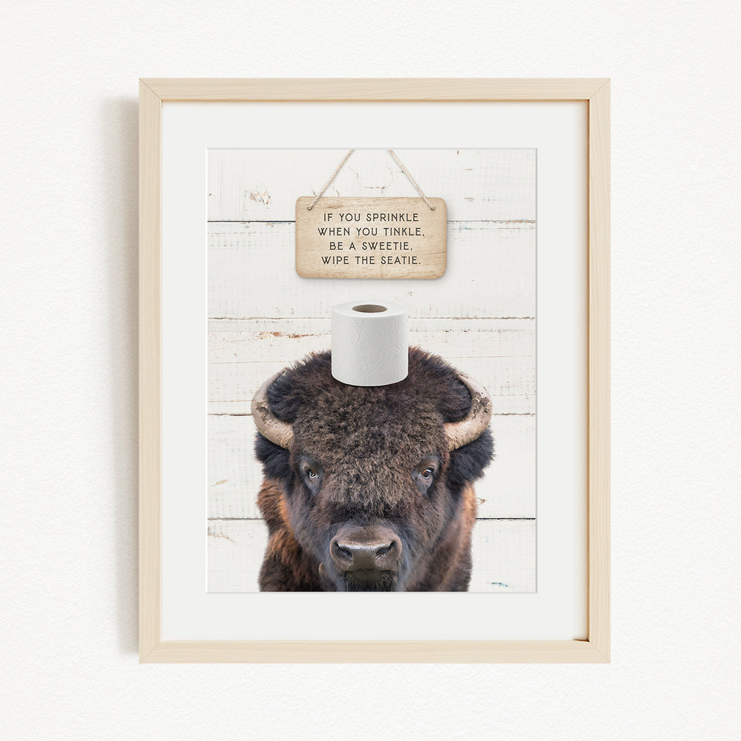 A framed image of a bison with a sign above it that reads "If you sprinkle when you tinkle, wipe the seattle".