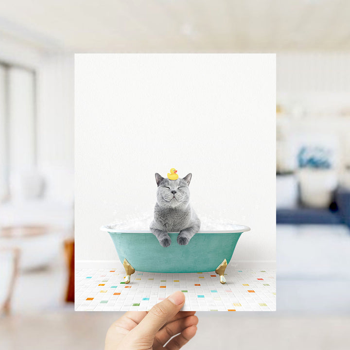 A gray cat sitting in a green bathtub, with a yellow rubber duck on its head, and a colorful tiled floor in the background.