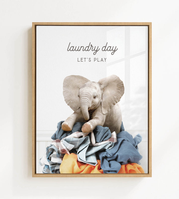 A framed image of a baby elephant sitting on a pile of laundry, with the text "laundry day let's play" written above it.