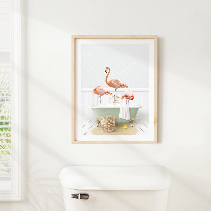 A framed image of three pink flamingos standing in a bathtub, with a basket of bath toys nearby.