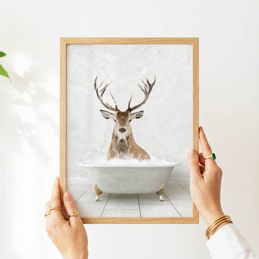 A person's hands are holding a framed picture of a deer in a bathtub, with the deer appearing to be enjoying the bath.