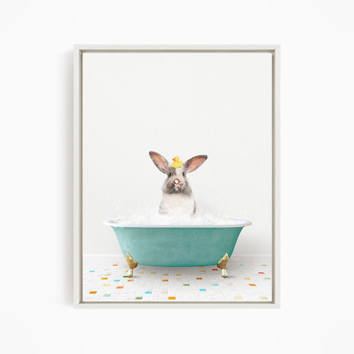 A gray and white rabbit sitting in a green bathtub filled with bubbles, with a yellow rubber duck floating on the water.