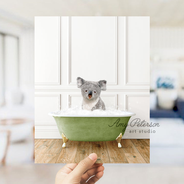 a hand holding up a photo of a koala in a bathtub