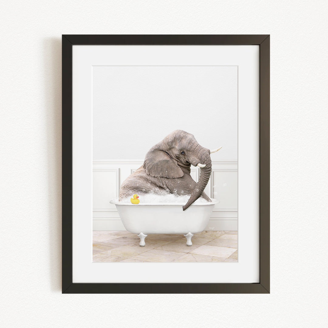 A gray elephant is sitting in a white bathtub, with a yellow rubber duck floating in the water.