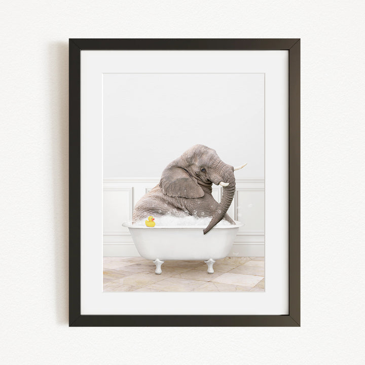A gray elephant is sitting in a white bathtub, with a yellow rubber duck floating in the water.