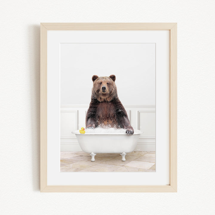 A brown bear sitting in a white bathtub, with a yellow rubber duck floating in the water.