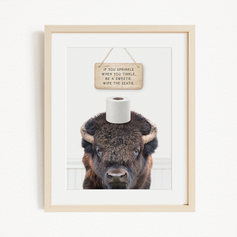 A framed image of a bison with a sign above it that reads "If you sprinkle when you tinkle, wipe the seattle".