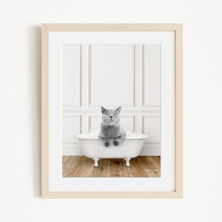 A gray cat sitting in a white bathtub, with a wooden floor and white paneled wall in the background.