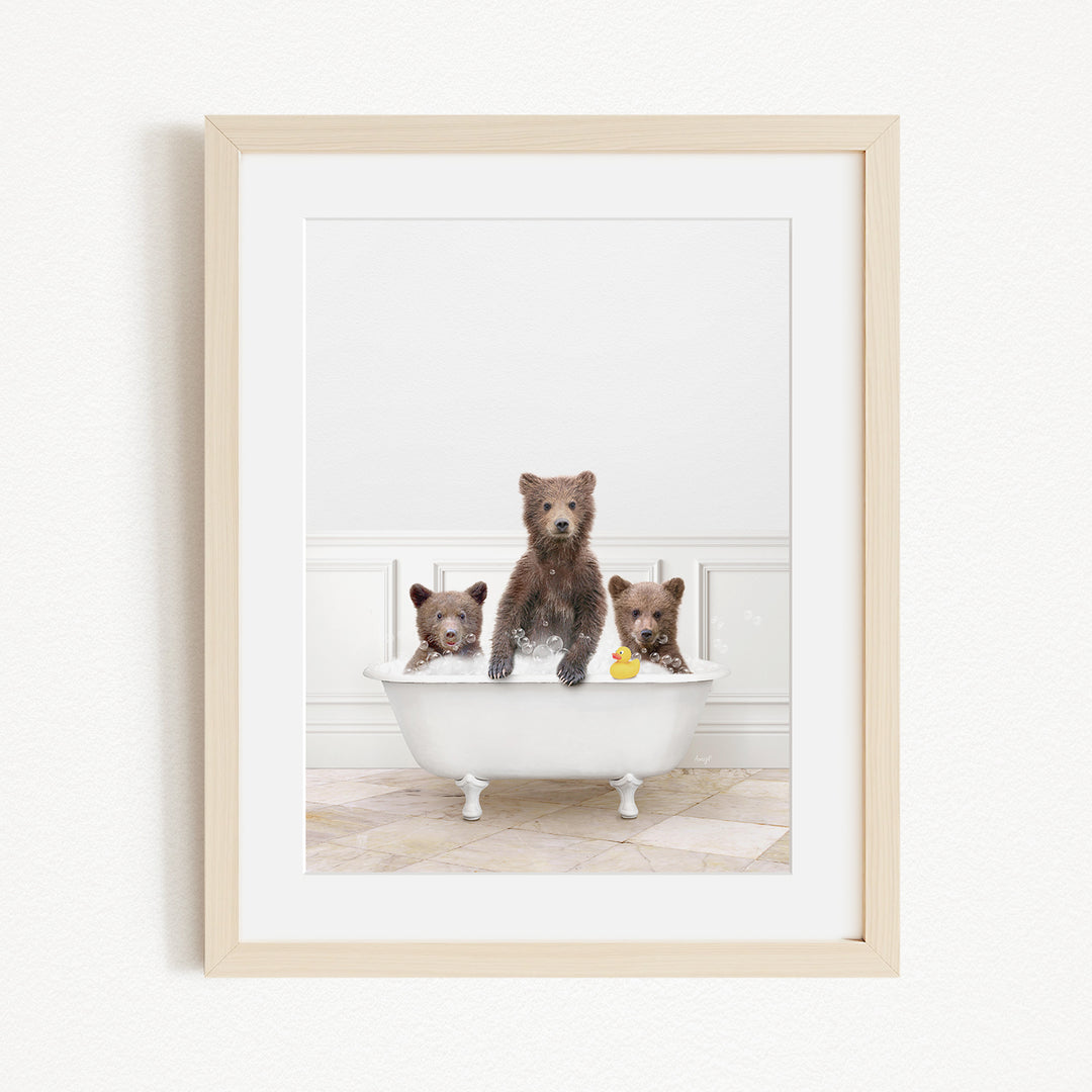 A framed image showing three brown bears sitting in a white bathtub, with one bear holding a yellow rubber duck.