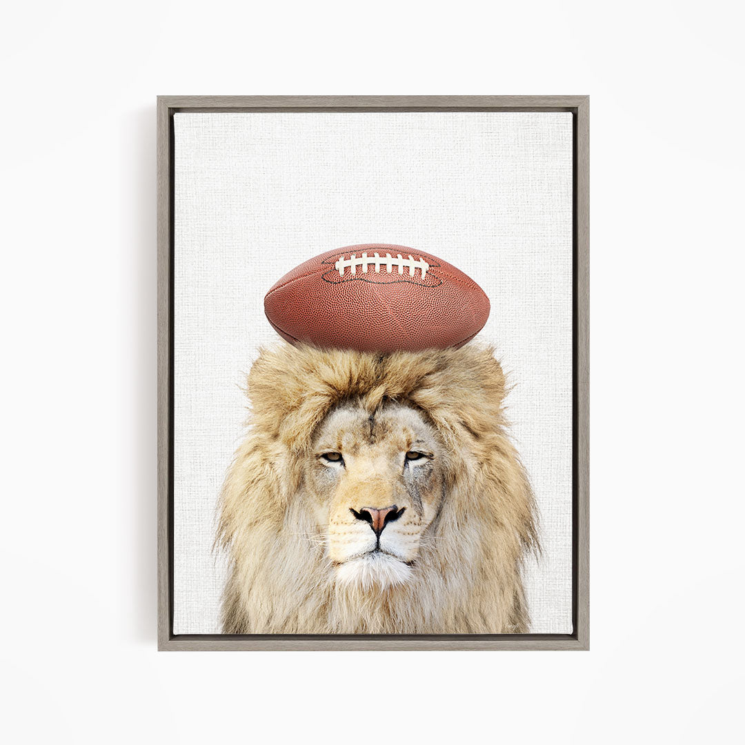 A lion with a football on its head, looking directly at the camera.