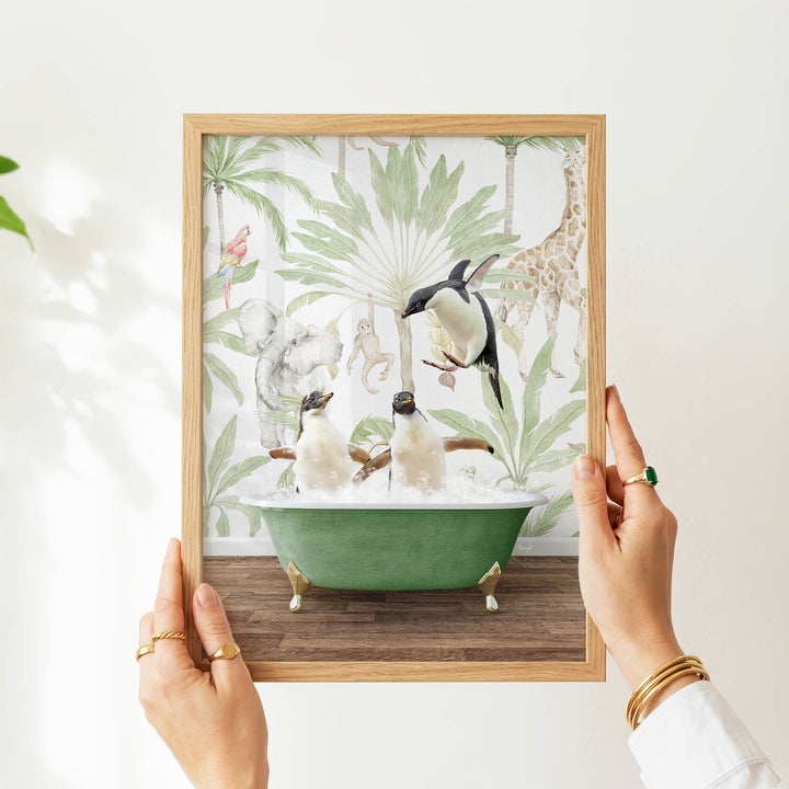 A person's hands are holding a framed picture of two penguins sitting in a green bathtub, surrounded by tropical foliage and animals.