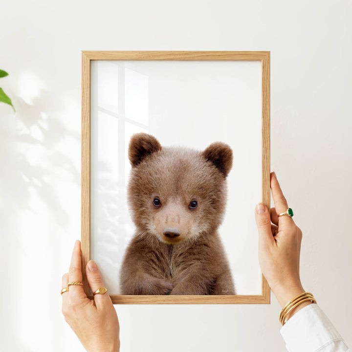 A person's hands are holding a wooden frame with a picture of a cute brown bear inside it.