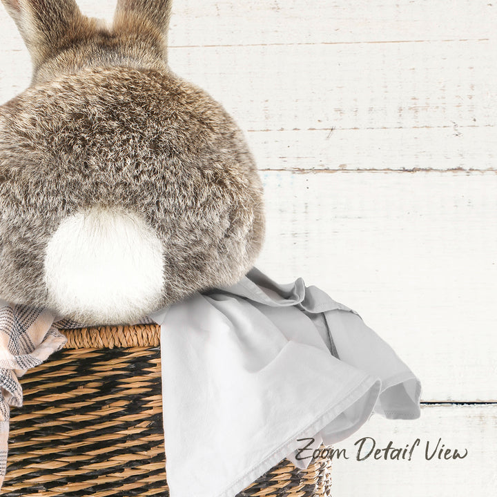 A fluffy gray rabbit sits atop a woven basket, with a gray blanket draped over it.