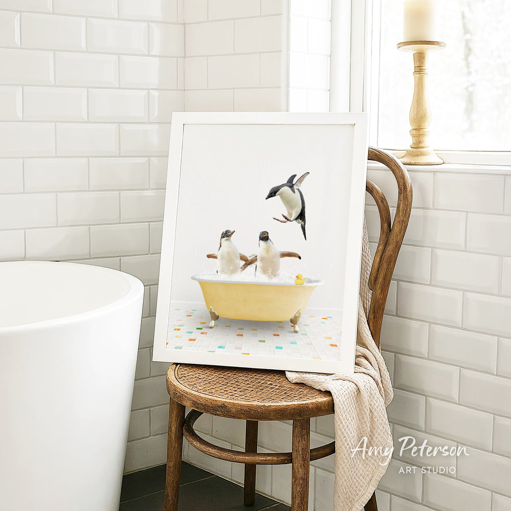 A framed image of two penguins sitting in a yellow bathtub, with one penguin standing on its hind legs and the other sitting comfortably.