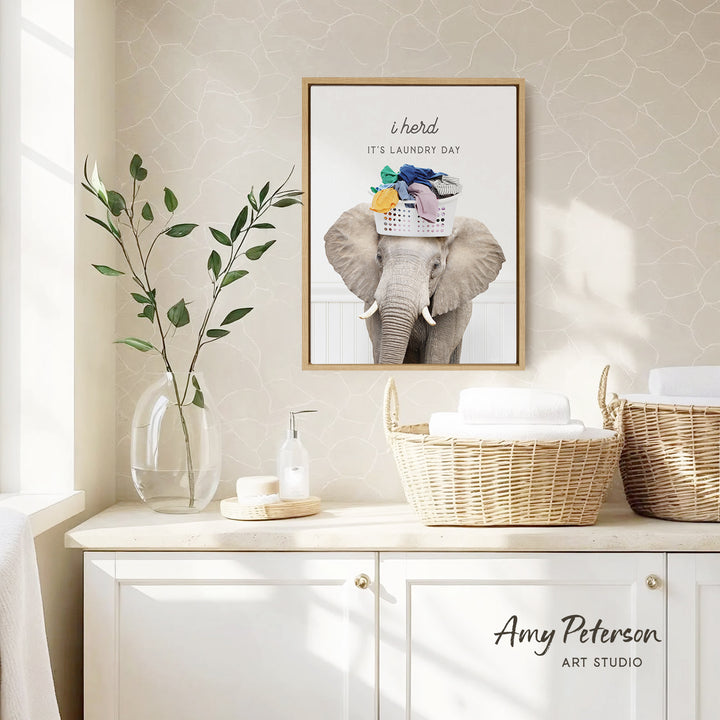 a framed poster of an elephant with a laundry basket on its head, hanging on a wall above a white cabinet.