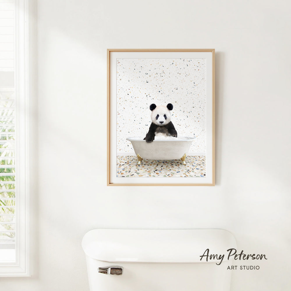 A framed image of a panda bear sitting in a bathtub, surrounded by confetti, is hanging on a white wall.