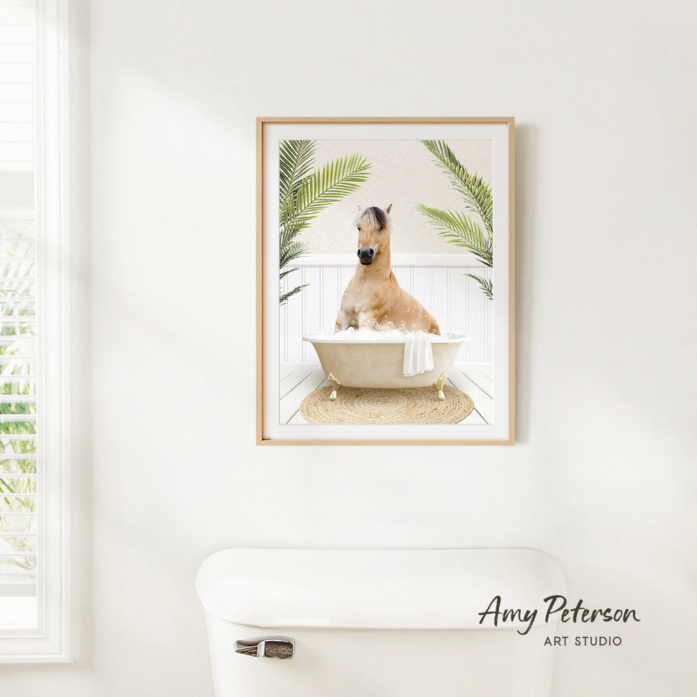 A framed image of a horse sitting in a bathtub, surrounded by palm leaves, is hanging on a white wall in a bathroom.