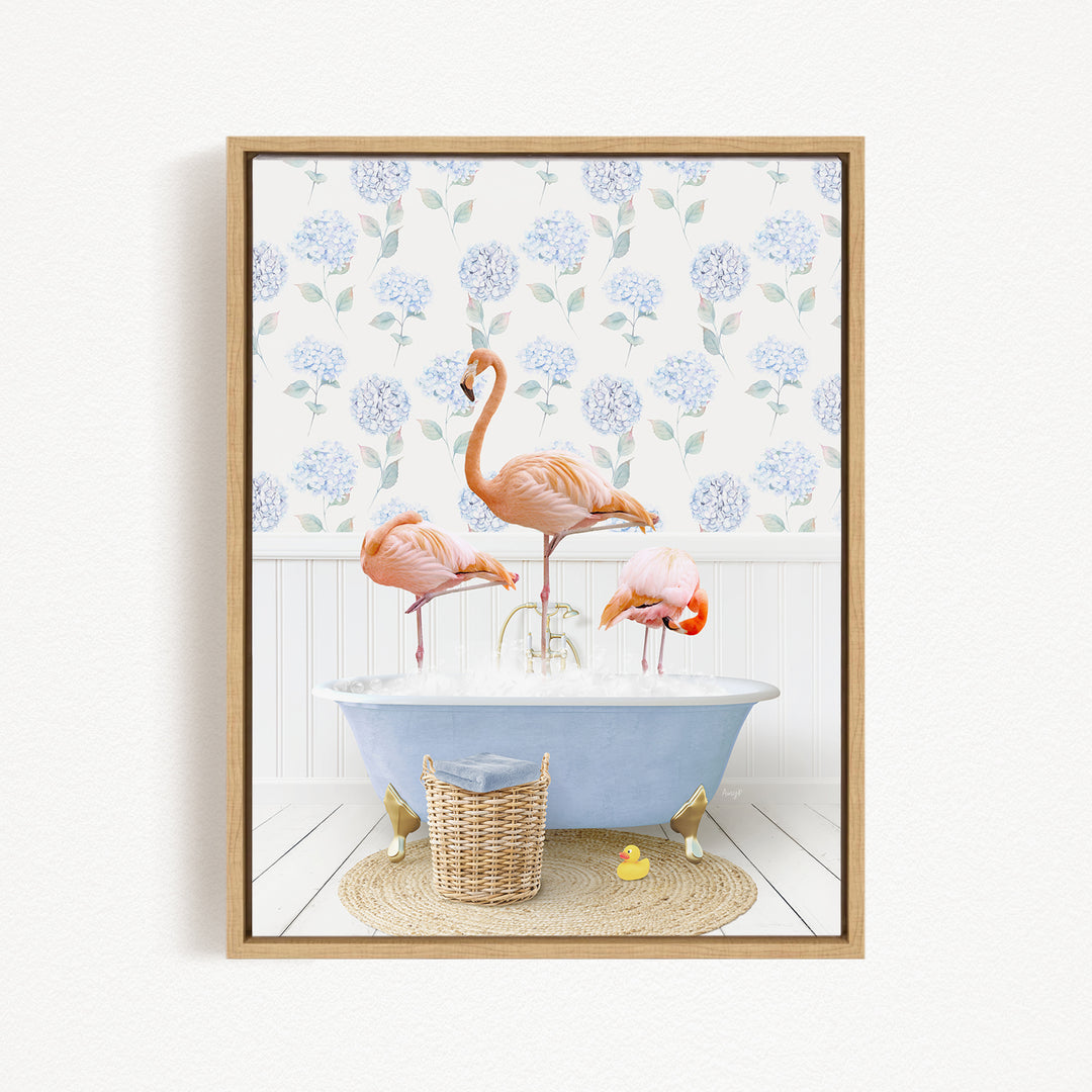 A framed image depicting three pink flamingos standing in a blue bathtub, with a blue and white floral wallpaper in the background.