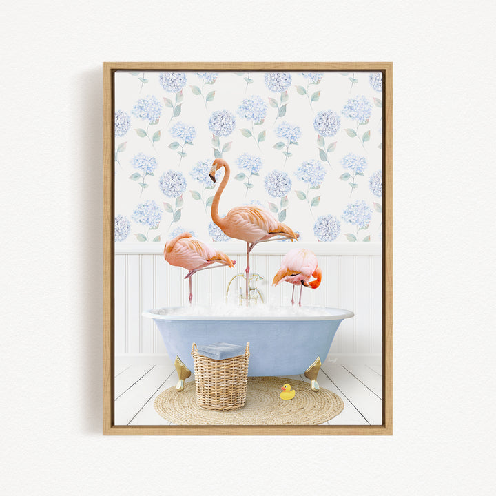 A framed image depicting three pink flamingos standing in a blue bathtub, with a blue and white floral wallpaper in the background.