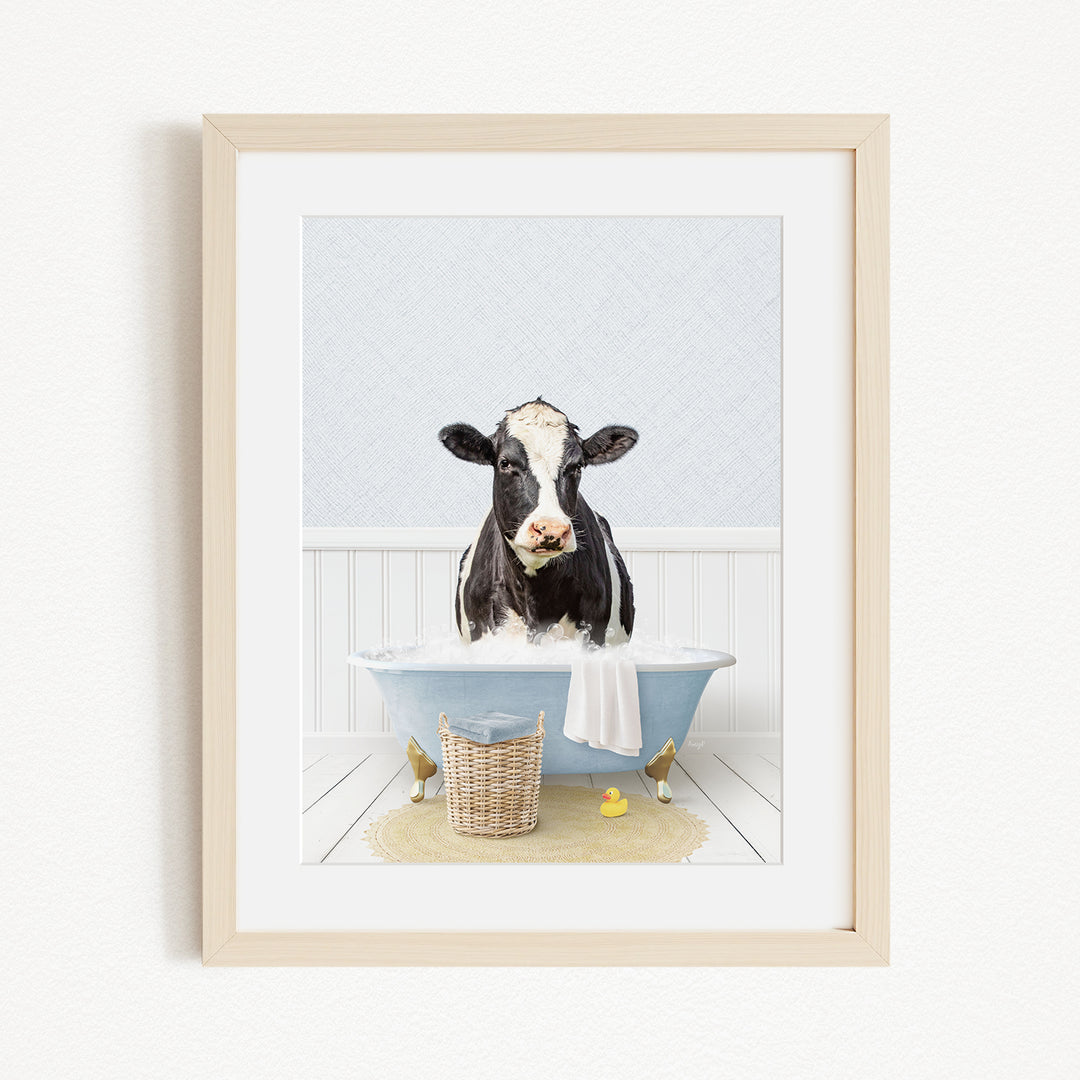 A black and white cow is sitting in a blue bathtub filled with water, surrounded by rubber ducks and a basket.