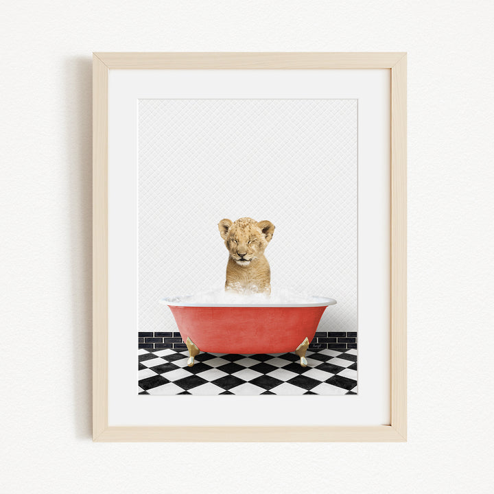 A young lion cub sitting in a red bathtub filled with water, surrounded by a black and white checkered floor.