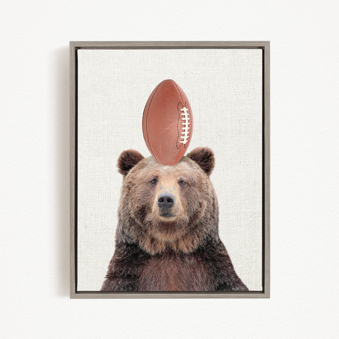 A brown bear standing on its head with a football on top of its head.