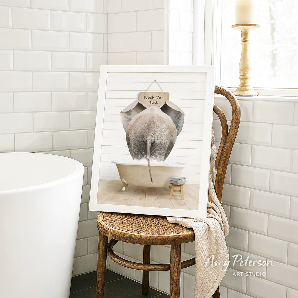 A framed image of an elephant sitting in a bathtub, with a sign above it that says "Wash Your Tail".