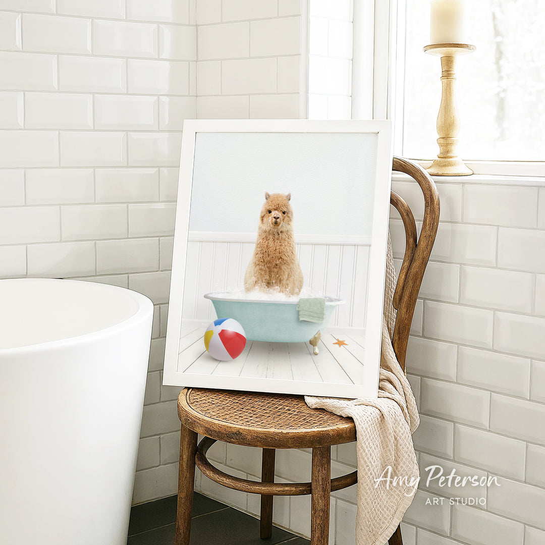 A framed image of a small dog sitting in a bathtub, surrounded by a beach ball and a towel, is displayed on a wooden chair in a bathroom setting.