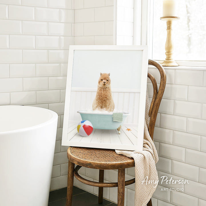 A framed image of a small dog sitting in a bathtub, surrounded by a beach ball and a towel, is displayed on a wooden chair in a bathroom setting.