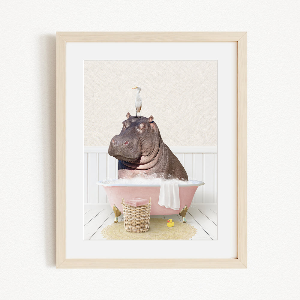 A framed image depicting a hippopotamus sitting in a pink bathtub, with a bird perched on its head.